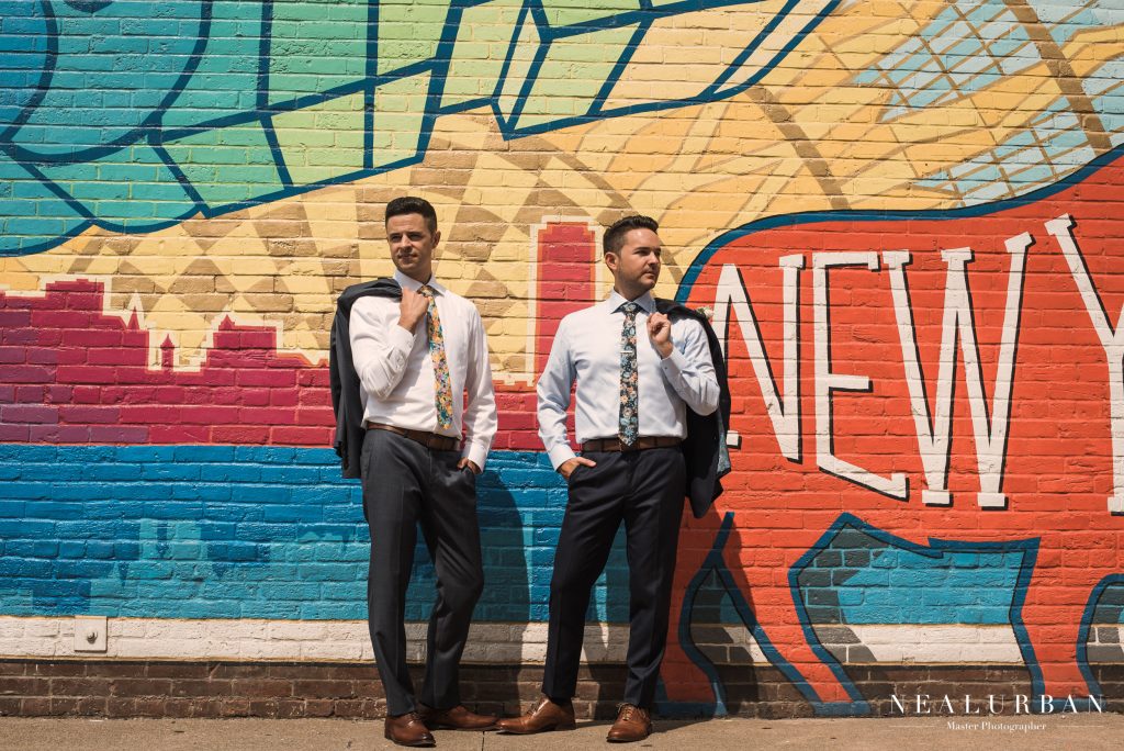 grooms posing in front of mural
